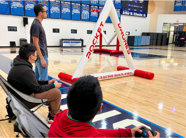 Students racing FPV drones in a school gym through Rocket Drones racing gates during an in-person competition.